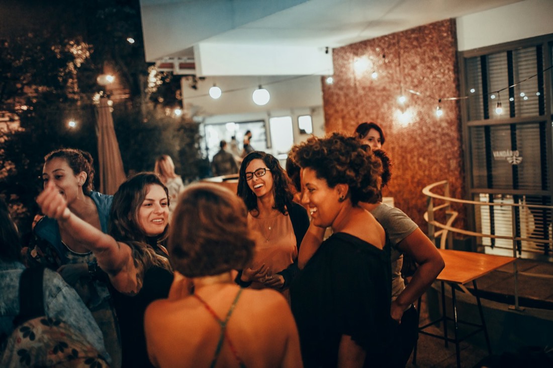Amigas riendo en la terraza de un bar pequeño de noche, bajo guirnaldas de luces