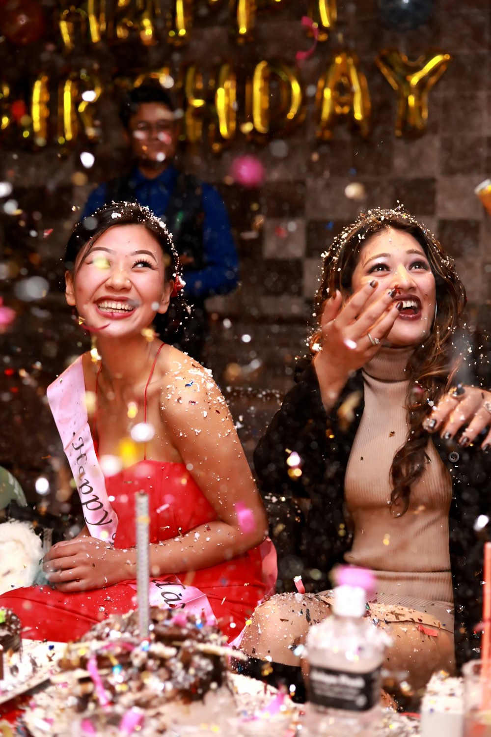 Dos amigas riendo bajo una lluvia de confeti en una fiesta de cumpleaños