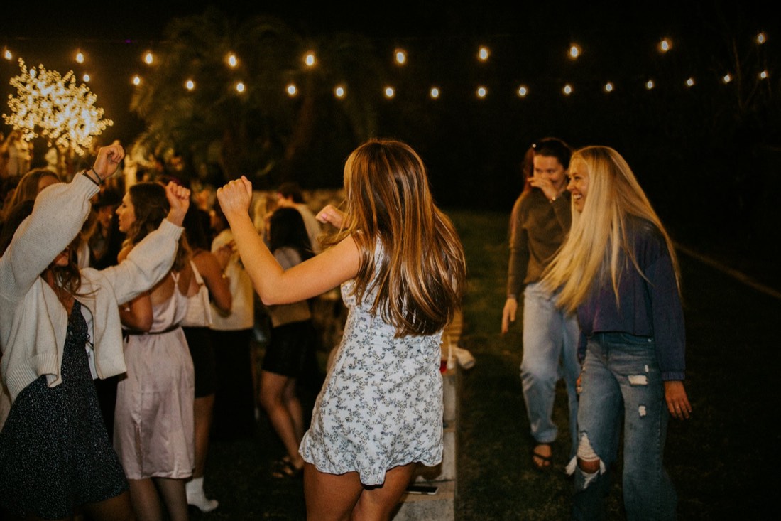 Amigas bailando de noche en un jardín bajo una guirnalda de luces
