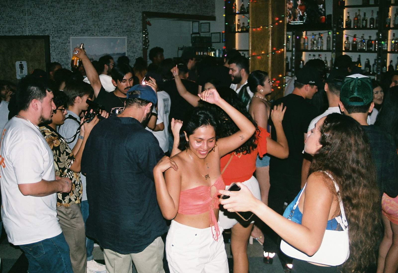 Amigos bailando en un bar pequeño, una de ellas con el móvil en la mano