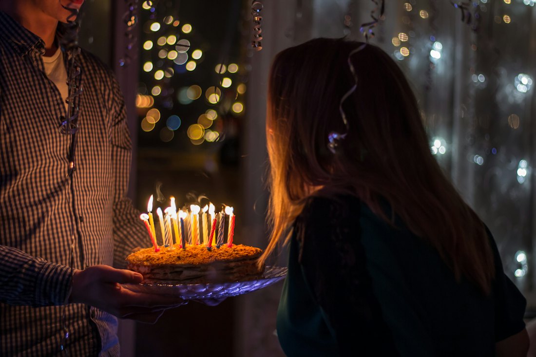 Un gâteau d'anniversaire aux bougies allumées tendu à une jeune femme, le soir