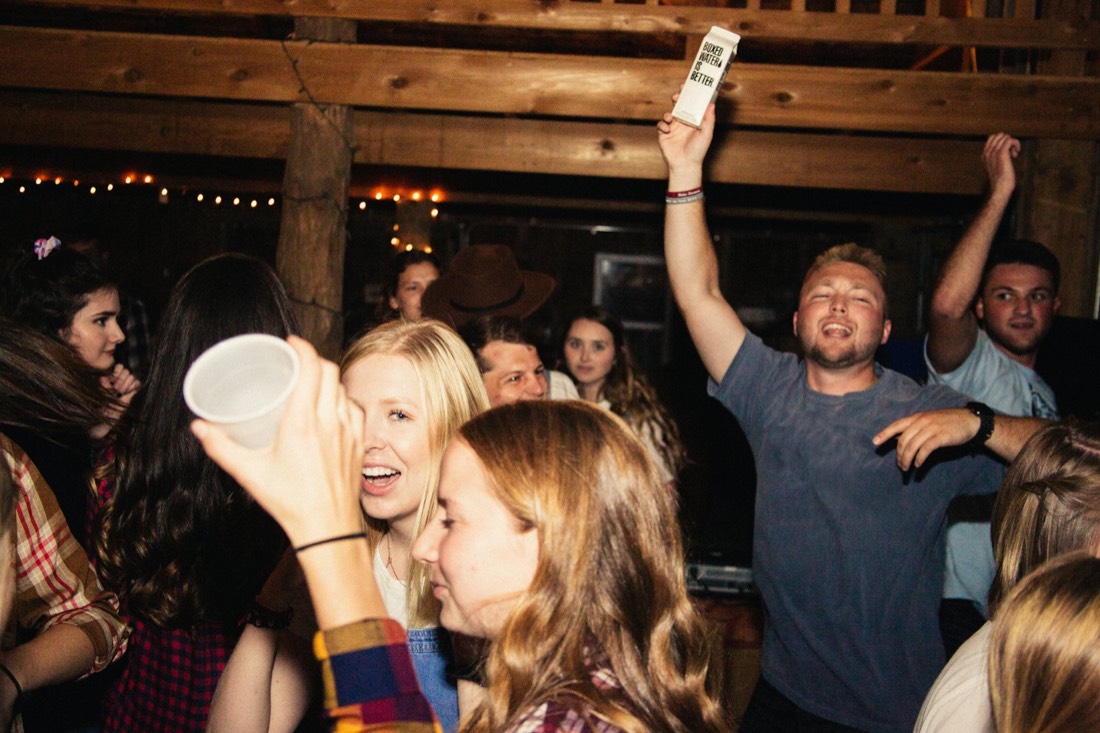 Friends dancing and cheering at a house party under string lights