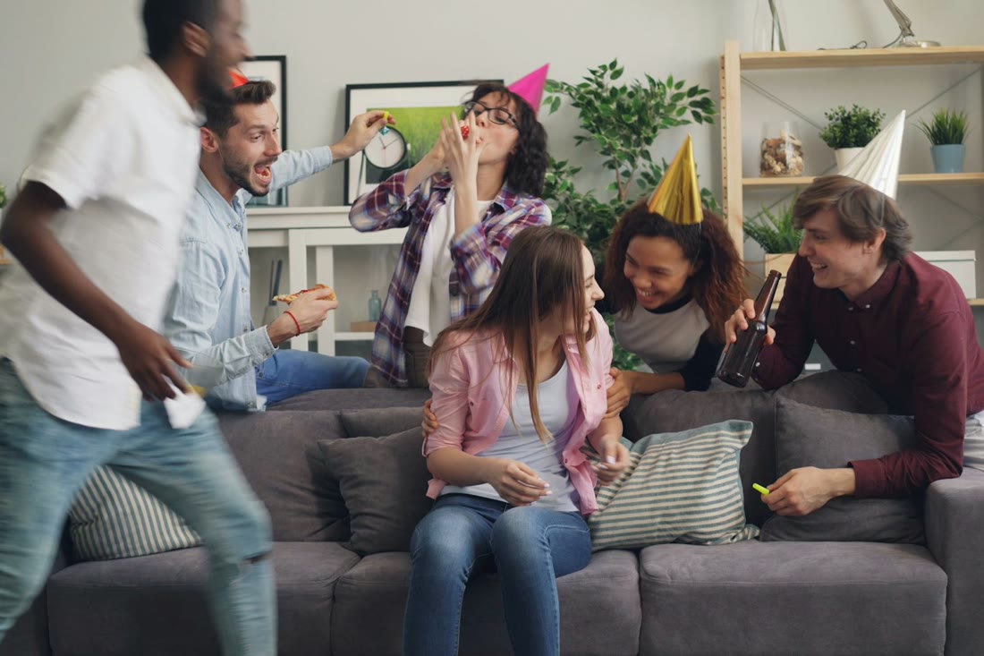 Friends in party hats laughing on a couch at home