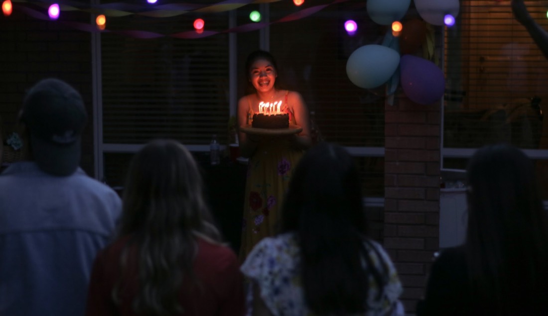 Friends gathered in the dark as a woman brings out a birthday cake with candles