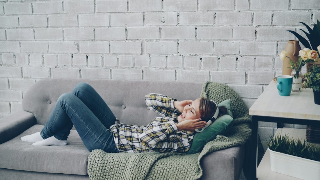 A woman lying on a sofa listening to music with headphones